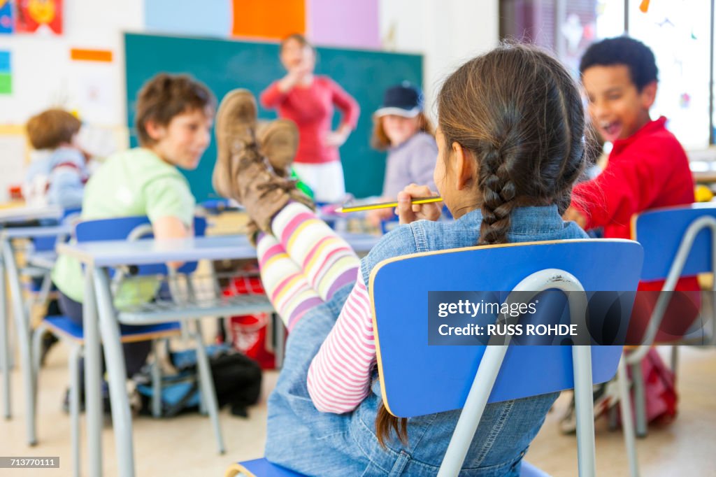 Rear view of primary schoolgirl with feet on desk in classroom