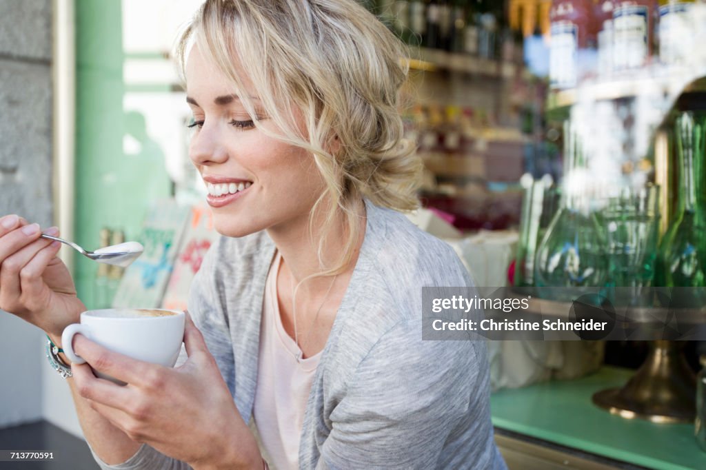 Mid adult woman eating froth from coffee cup at city sidewalk cafe