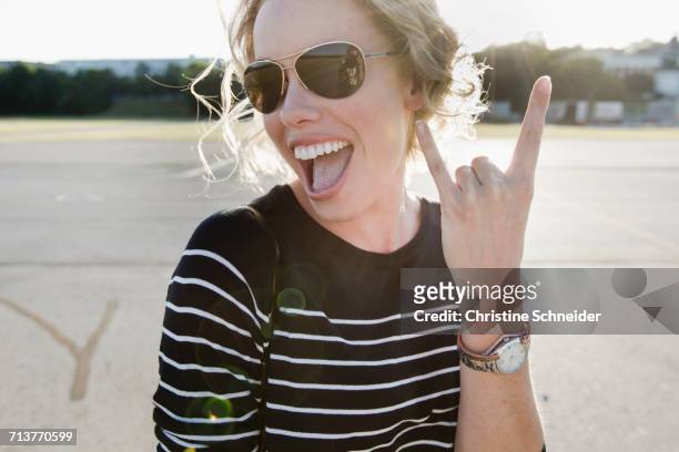 portrait of mid adult woman wearing sunglasses making i love you hand gesture - pilotenbrille stock-fotos und bilder