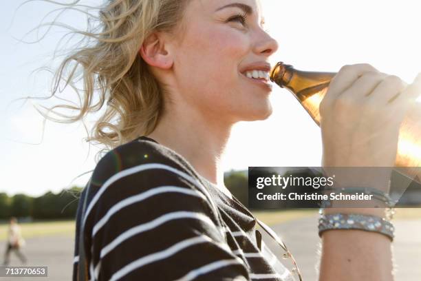 mid adult woman drinking bottled beer outdoors - beer stock-fotos und bilder