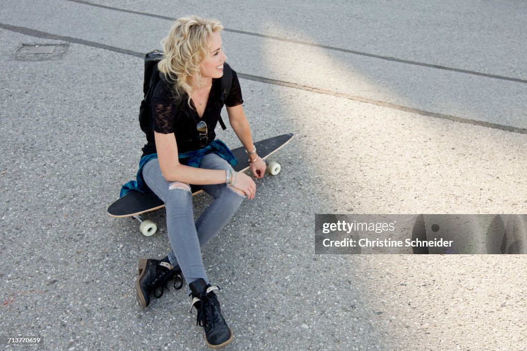 Female skateboarder sitting on skateboard