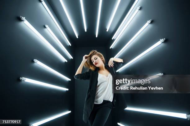 young fashion model posing in studio, electric lighting behind her - luce fluorescente foto e immagini stock