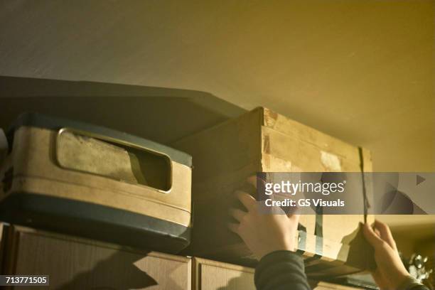 hands of boy reaching to remove cardboard box from shelves - cellar stockfoto's en -beelden