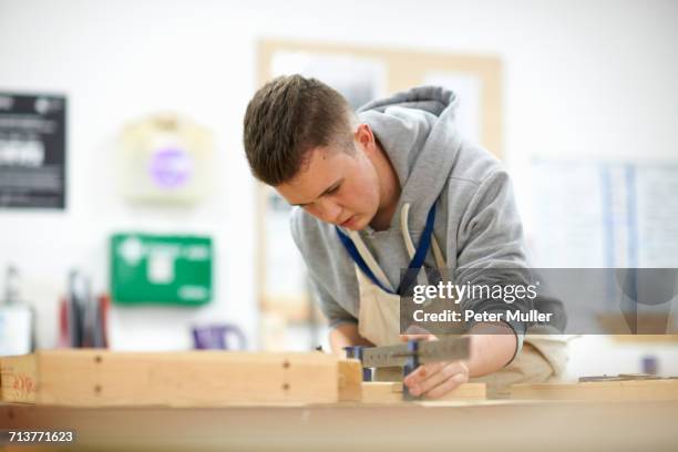 male teenage carpentry student adjusting wood clamp in college workshop - ausbildung und tischler stock-fotos und bilder