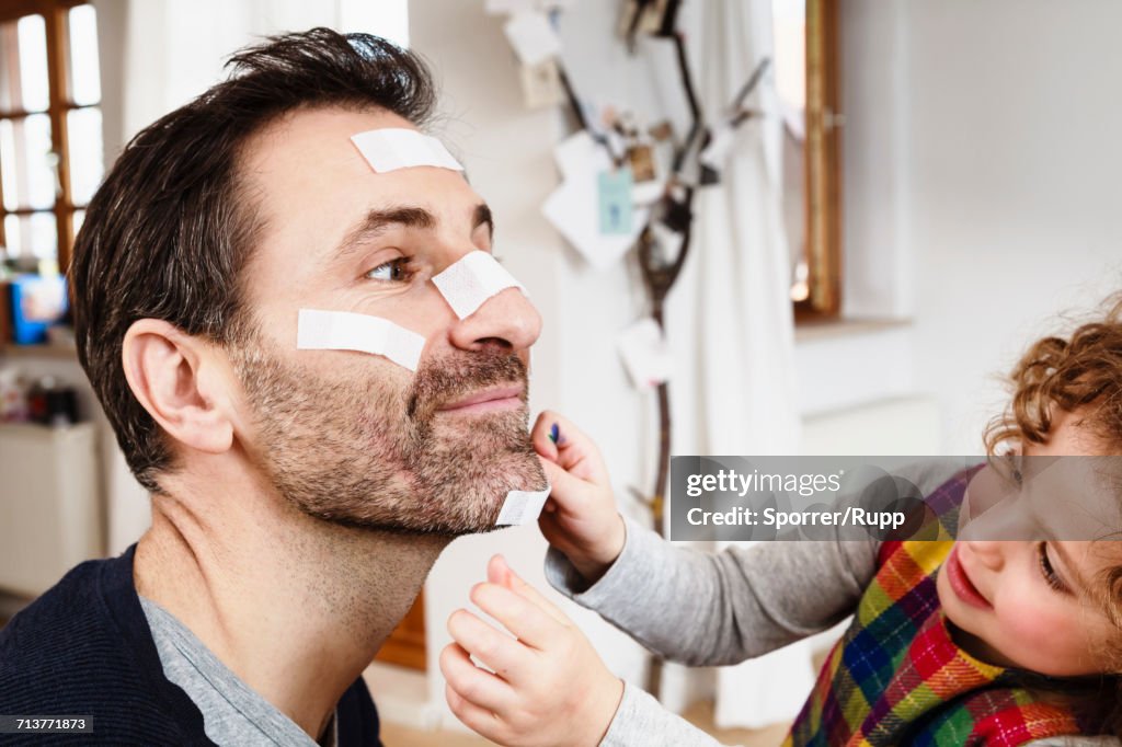 Girl sticking adhesive plaster onto fathers chin