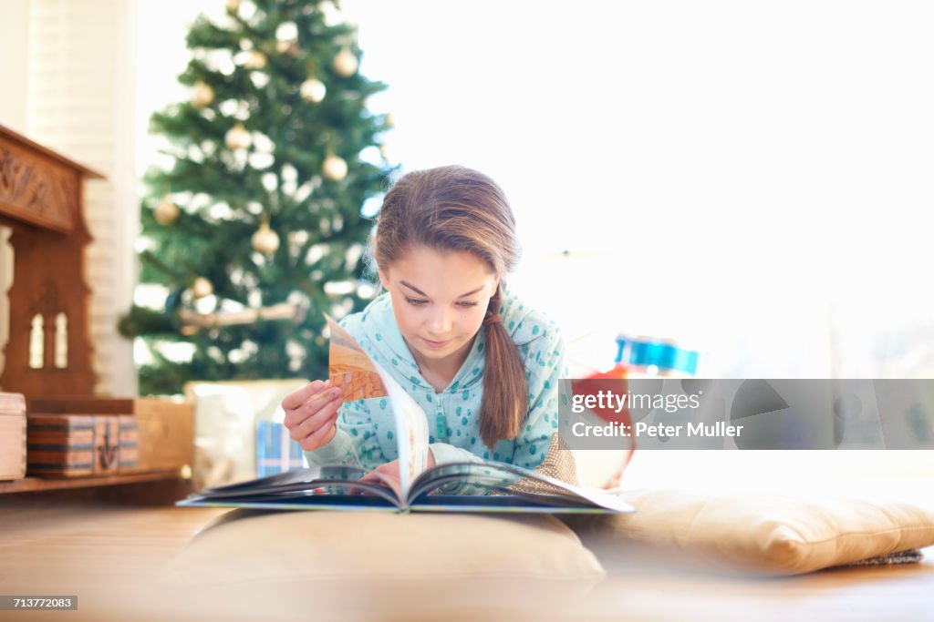 Girl lying on living room floor reading book at christmas