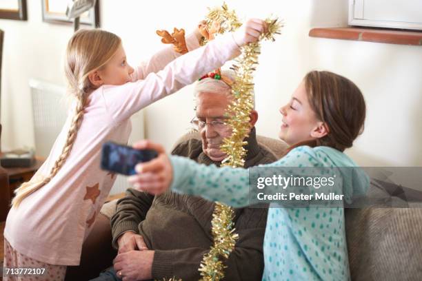 sisters taking smartphone selfie while putting tinsel on sleeping grandfather - christmas funny stockfoto's en -beelden