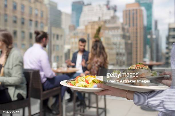 waitress holding dishes while friends sitting against glass window at restaurant - waiter new york stock pictures, royalty-free photos & images