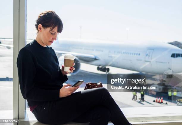 woman using phone while sitting at airport - airplane phone stock-fotos und bilder