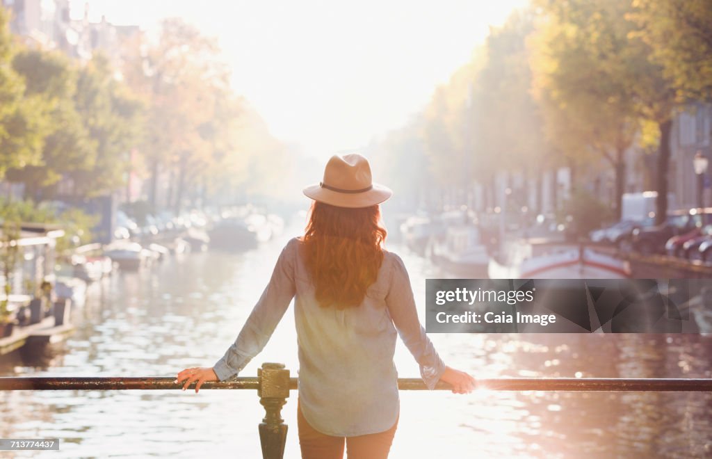 Woman wearing hat looking at sunny autumn canal view, Amsterdam