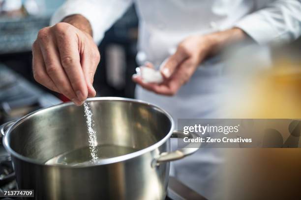 chef putting salt in pan of water on stove, close-up - close up cooking stock-fotos und bilder