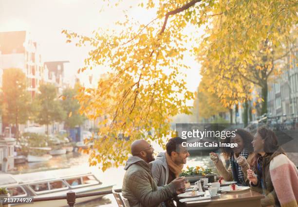 friends laughing and eating cheesecake dessert at autumn sidewalk cafe along canal, amsterdam - amsterdam people stock pictures, royalty-free photos & images