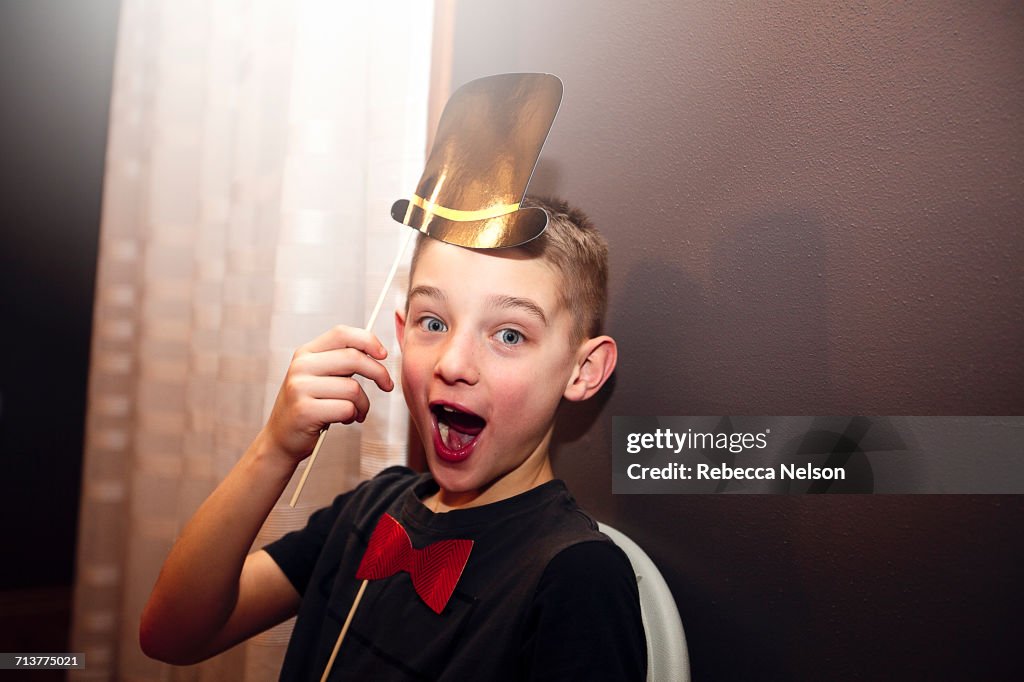 Portrait of boy holding bow tie and top hat stick masks posing at party