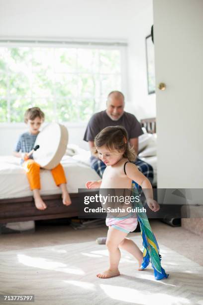 brother drumming on bed, sister playing superhero while father watch on - baby being held stockfoto's en -beelden