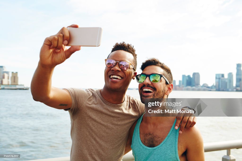 Two young men taking smartphone selfie on waterfront, New York, USA