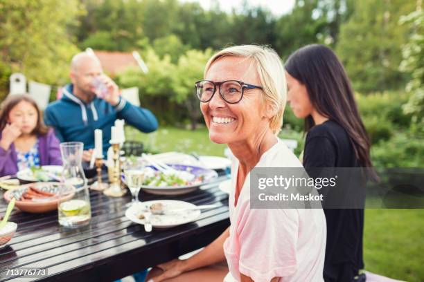 happy woman sitting with friends and family at dining table in back yard during garden party - family back yard stockfoto's en -beelden