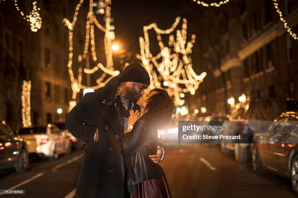 Romantic couple kissing by Christmas lights at night, New York, USA