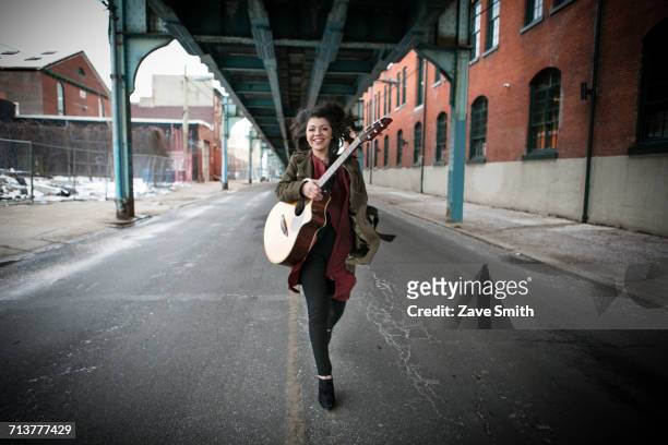 young woman running below elevated road with acoustic guitar - musician portrait stock pictures, royalty-free photos & images