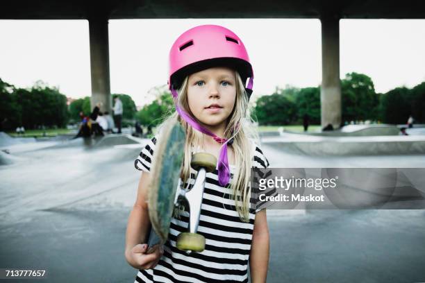 portrait of girl holding skateboard while standing at park - child skating stock pictures, royalty-free photos & images