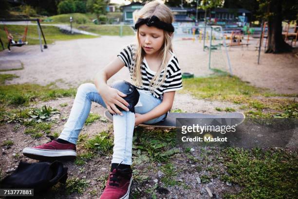 girl tying kneepad while sitting on skateboard at park - kniebeschermer stockfoto's en -beelden