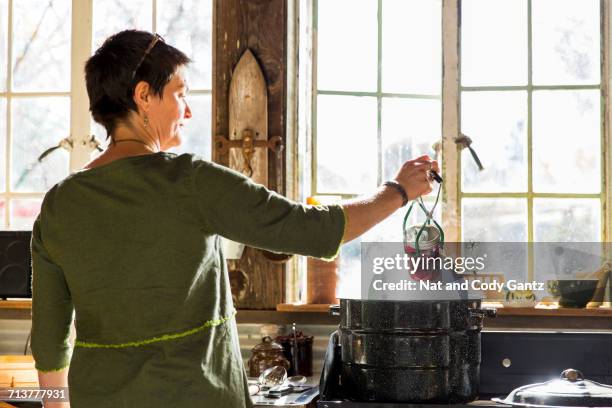 rear view of woman removing beetroot preserves jar from steaming saucepan - in konserve abfüllen stock-fotos und bilder