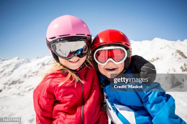 cheerful siblings in ski-wear standing against snowcapped mountain - gafas de esquí fotografías e imágenes de stock