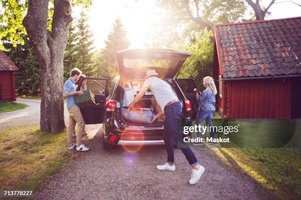 full length of friends loading luggage into car on road during sunny day - car trunk - fotografias e filmes do acervo