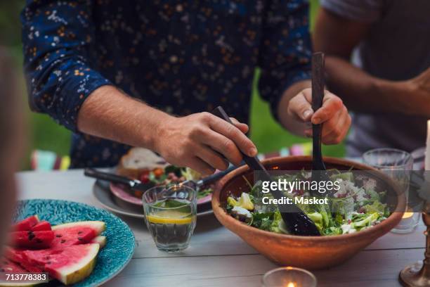 midsection of man mixing salad at table during garden party - portion imagens e fotografias de stock
