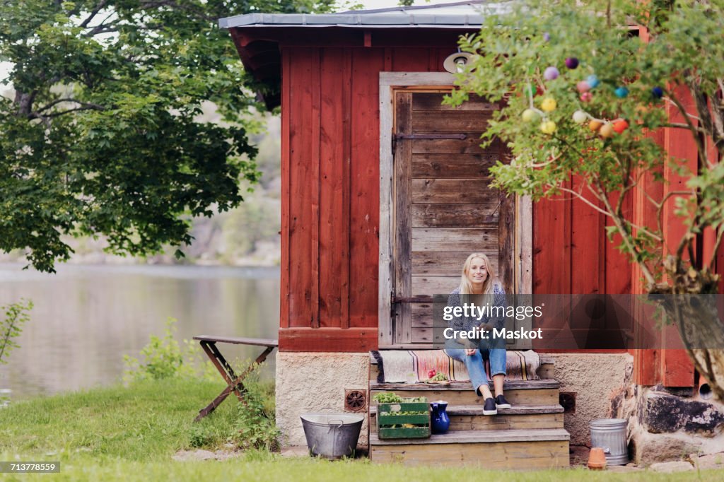 Smiling woman with organic vegetable sitting outside wooden cottage