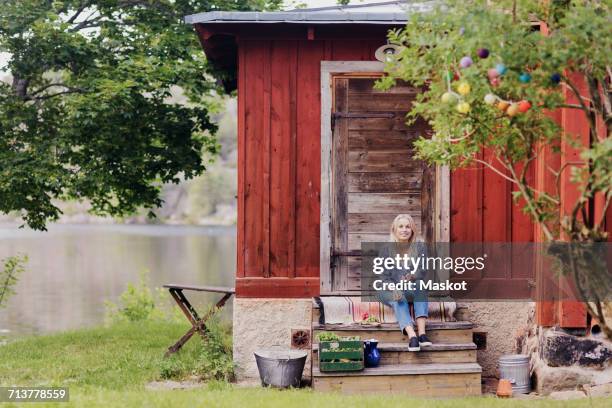 smiling woman with organic vegetable sitting outside wooden cottage - cottage bildbanksfoton och bilder