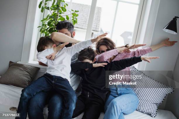 cheerful family doing dab while sitting on sofa in living room at home - dab dance stock pictures, royalty-free photos & images