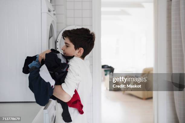side view of boy carrying clothes by washing machine at home - carrying laundry stock pictures, royalty-free photos & images