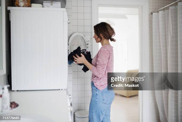side view of woman loading clothes in washing machine at home - laundry persons stock pictures, royalty-free photos & images
