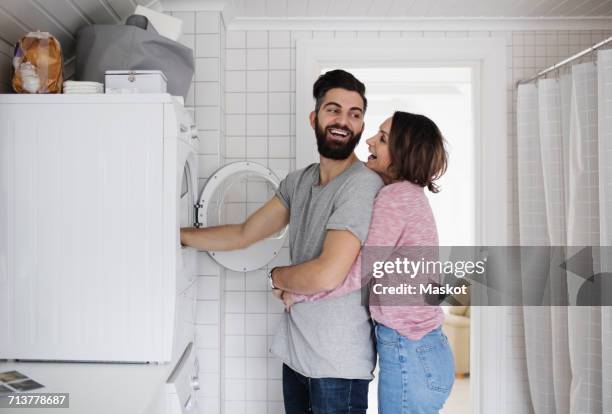 happy couple standing by washing machine at home - couples showering 個照片及圖片檔