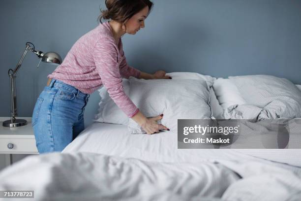 side view of woman arranging pillows on bed at home - bettbezug stock-fotos und bilder