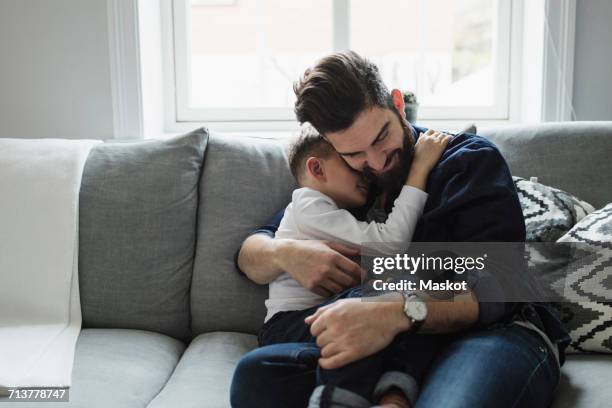 father embracing son while sitting on sofa at home - arab family happy photos et images de collection
