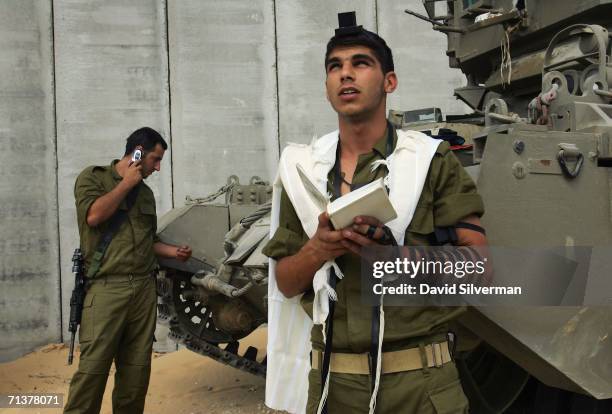 An Israeli soldier recites his Jewish morning prayers as a crew mate calls home shortly after their armored personnel carrier left the Gaza Strip to...