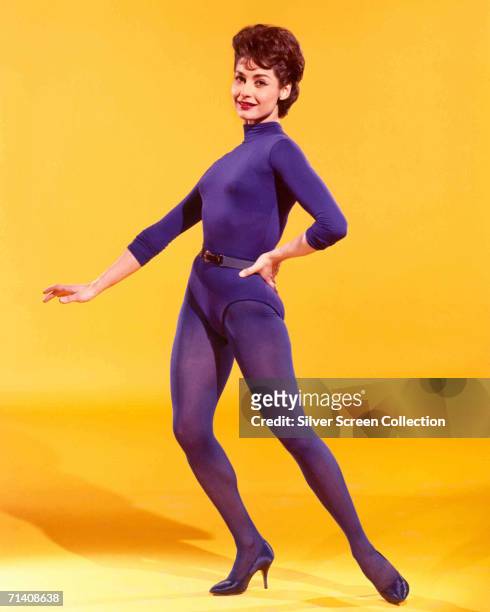 American actress Carol Lawrence wearing a purple leotard and matching tights against a yellow backdrop, circa 1960.