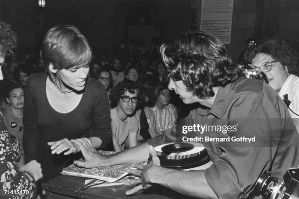 American peace activist and later politician Tom Hayden pushes back his wife, actress and activist Jane Fonda, as he protects a slide projector...