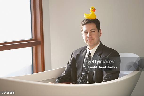 hispanic businessman sitting in a bathtub with a rubber ducky on his head - おもちゃのアヒル ストックフォトと画像