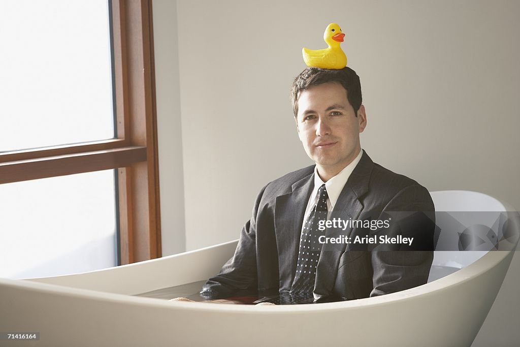 Hispanic businessman sitting in a bathtub with a rubber ducky on his head