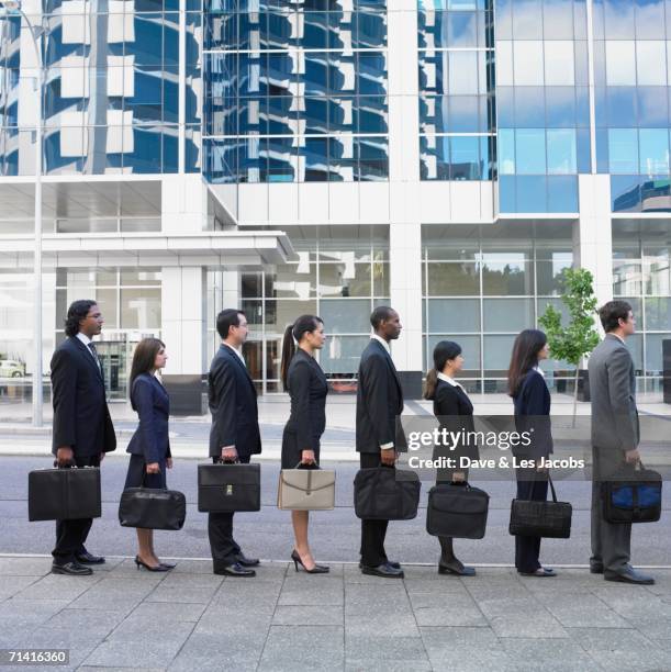 line of businesspeople holding briefcases outdoors - businessman in black suit photos et images de collection