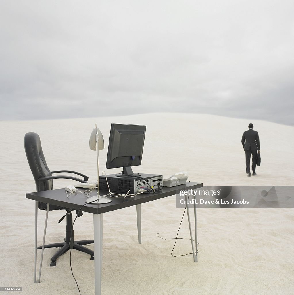Businessman walking away from desk in the desert