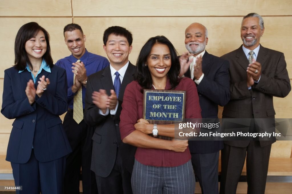 Businesswoman holding Employee of the Month plaque with co-workers applauding