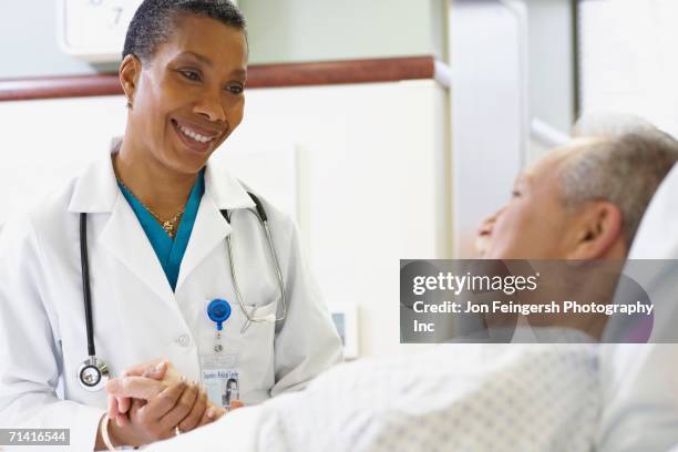 african female doctor with patient in hospital bed - man and woman holding hands profile stock-fotos und bilder