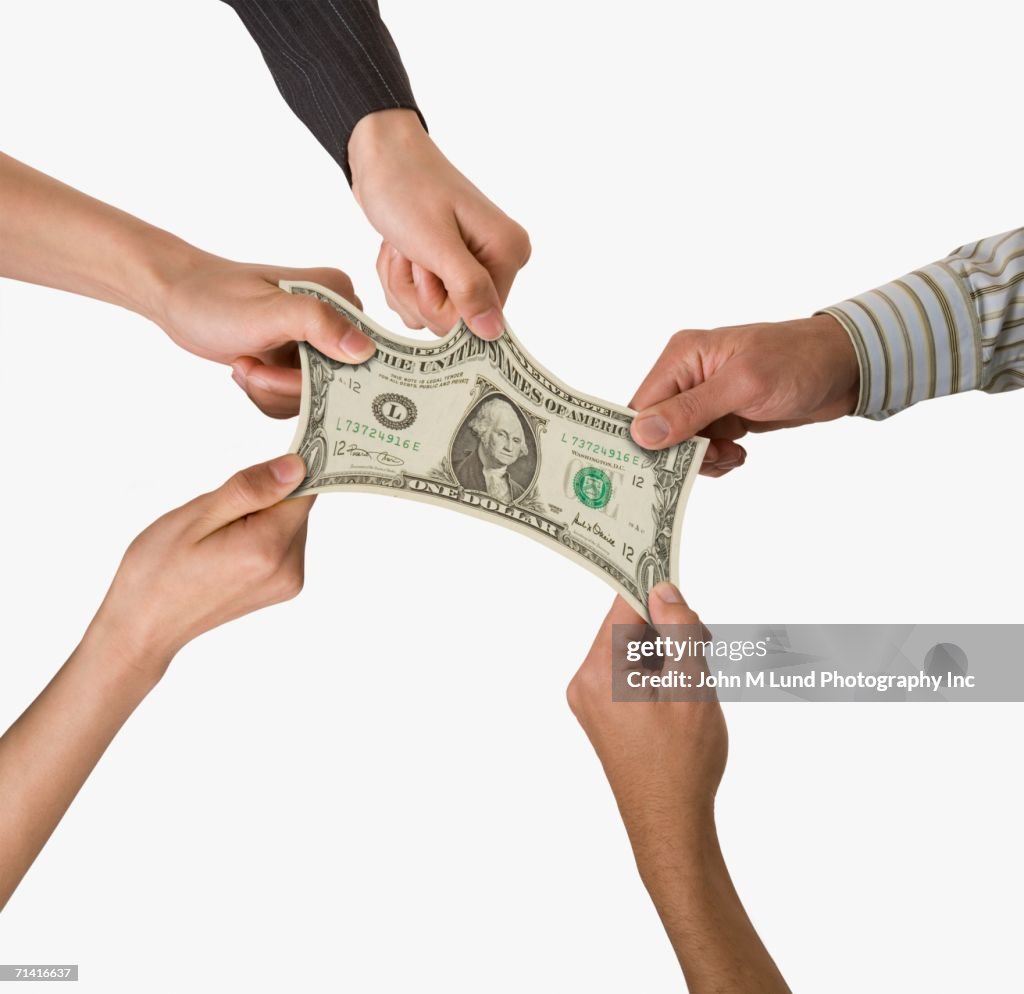 Studio shot of people's hands pulling on dollar bill