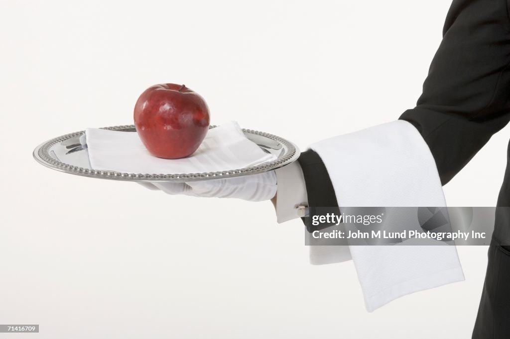 Butler holding a silver tray with an apple