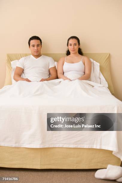 hispanic couple sitting in bed - junge frau bett sitzen blick in die kamera stock-fotos und bilder