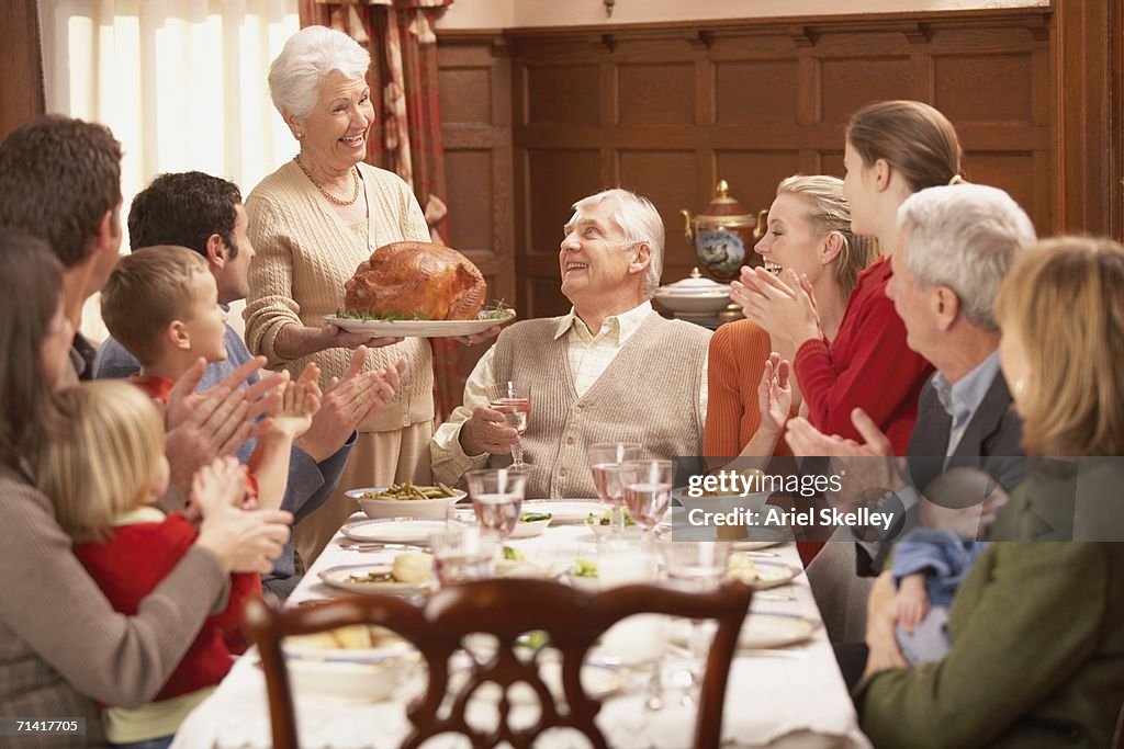 Grandmother presenting turkey to her family at the dinner table