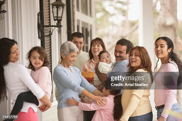 hispanic grandmother hugging her granddaughter with family around - 家族の集まり ストックフォトと画像